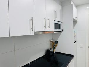 a white kitchen with a microwave and a sink at Aladín House Vinaròs playa in Vinarós +2 photos