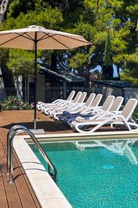 a row of chairs and an umbrella next to a pool at Waterman Beach Village in Supetar