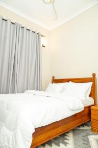 a white bedroom with a wooden bed with white sheets at Magnolia Homes Tz in Nkunjila +7 photos