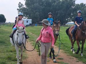a group of children riding on horses with a woman at Buitehof Gasteplaas in Stewartby