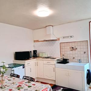 eine Küche mit weißen Schränken und einem Waschbecken und einem Tisch in der Unterkunft La maison de la cité médiévale in Donzenac