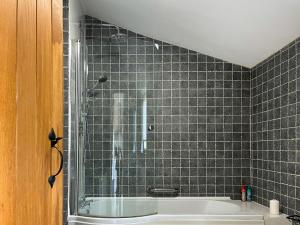 a bathroom with a tub and a tiled wall at Ravenscliffe Cottage in Tissington +2 photos