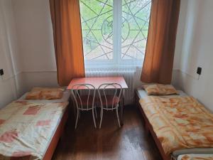 a room with two beds and a table and a window at Alexander Munkásszálló Oroszlány in Oroszlány