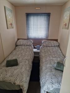 two beds in a small room with a window at 6 Berth Caravan For Hire In Essex, Seawick Holiday Park Ref 27016R in Clacton-on-Sea +10 photos