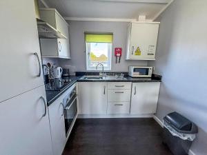 a small kitchen with white cabinets and a sink at Charming Chalet On A Fantastic Holiday Park In Lowestoft Ref 12077B in Lowestoft +8 photos