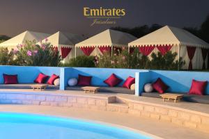 斋沙默尔Emirates Luxury Desert Camps的配有沙发、桌子和遮阳伞的游泳池