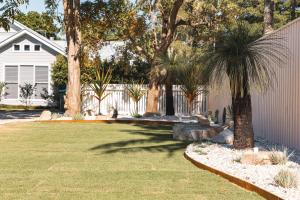 a yard with palm trees and a white fence at The Little Tropicana in Byron Bay