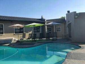 a swimming pool with chairs and umbrellas next to a house at URlyfstyle Cottage 10km from OR Tambo Int Airport in Kempton Park