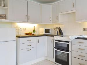 a white kitchen with white cabinets and a stove top oven at Church Court Cottage in Beeford