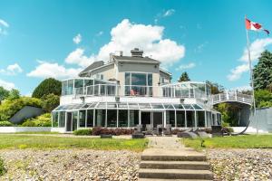 une grande maison blanche avec des fenêtres en verre et un drapeau dans l'établissement Lakefront Wellness Estate - Pool, Sauna and Hot Tub, à Lac-Simon