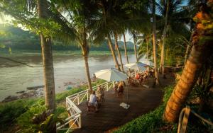 a group of people sitting under umbrellas on a dock near a river at The Belle Rive Boutique Hotel in Luang Prabang