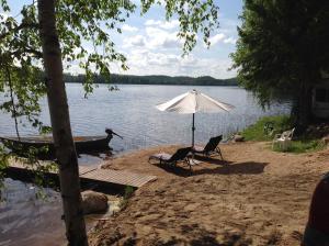 a beach with two chairs and an umbrella and a boat at Tilhi 1 Cottage in Piojärvi