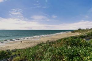 a beach with people walking on the sand and the ocean at Cottesloe Neue Blue Apartment in Perth