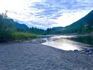 a river with a rocky shore with trees and mountains at Nord-Garthus gård leilighet 1 in Hølera +5 photos