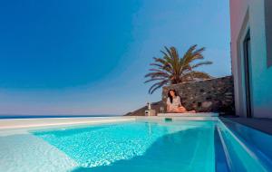a woman sitting on a wall next to a swimming pool at Luxury Santorini Villa Villa Elysian Pente Private Pool 2 Bedrooms in Foinikiá