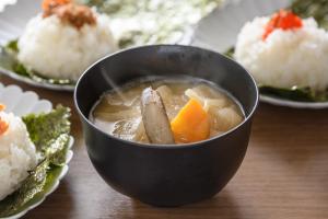 a bowl of soup with vegetables and rice on a table at Via Inn Shin Osaka in Osaka