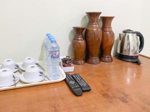 Una mesa con un control remoto y tazas y jarrones. en Hotel Permai Syariah RedPartner Sananwetan Blitar, en Karangtengah