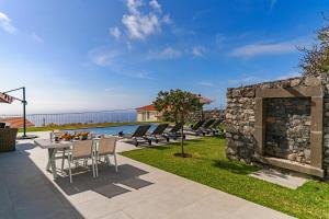 a patio with a table and chairs next to a stone wall at Luxury Calheta Villa Casa Calheta Heights 3 Bedrooms Stunning Sea Views in Calheta