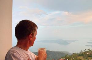 un homme tenant une tasse donnant sur une fenêtre dans l'établissement Blowing in the Wind - Lake View Apartments, à Tagaytay