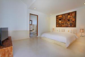 a white bedroom with a bed and a television at Love Is Simple Bali in Canggu