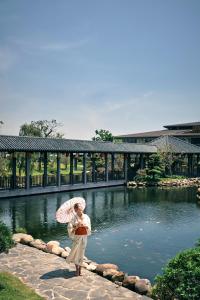 a woman with an umbrella standing in front of a pond at Kobi Onsen Resort Hue, Affiliated by Melia in Hue