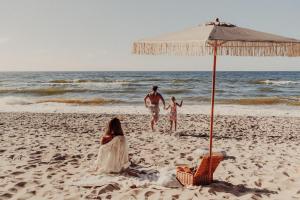 Ein Mann und zwei Kinder am Strand unter einem Sonnenschirm in der Unterkunft Hotel Linea Mare in Pobierowo
