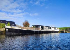 ein Boot auf dem Wasser mit einem Haus darauf in der Unterkunft 8 Personen Hausboot mit Hot Tub, Sauna, Kaminofen, Klimaanlage, Lounge, Sonnendeck und Garten mit Buddelschiff direkt hinterm Deich in Otterndorf in Otterndorf
