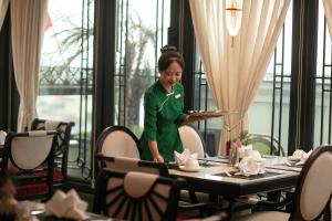 a woman in a green uniform standing in a restaurant at La Mejor Indochine Hotel in Hanoi