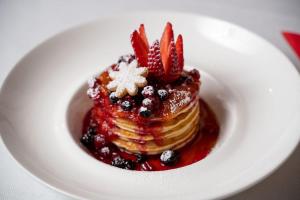 a white plate with a stack of pancakes with syrup and berries at La camera degli Specchi Piazza Unità D'Italia in Trieste