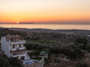 a house on a hill with the sunset in the background at Luxurious Villa Kirianna - Private Pool, Jacuzzi, Sauna, & Gym - 13km to Rethymno center in Kiriánna