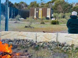 a woman sitting in front of a fire pit at Dunalley Bay Beachfront Retreat by Tiny Away in Murdunna