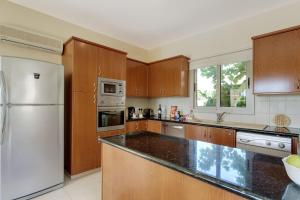 eine Küche mit Holzschränken und einem weißen Kühlschrank in der Unterkunft Luxury Coral Bay Villa Villa Shanta 3 Bedroom Villa Distant Sea Views in Peyia