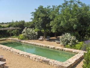 une piscine dans un jardin avec des bancs et des arbres dans l'établissement Maison d'Hôtes Mas de Barbut, à Saint-Laurent-dʼAigouze