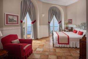 a bedroom with a bed and a chair and windows at Hotel Caesar Augustus in Anacapri