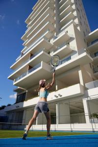 a woman holding a tennis racket in front of a building at Mediterranean Beach Hotel in Limassol