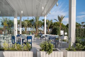 a restaurant with white tables and blue chairs and palm trees at Voyage Belek Golf & Spa Hotel in Belek