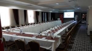 una lunga fila di tavoli in una stanza con un uomo su uno schermo di Grand Cali Hotel a Bozuyuk