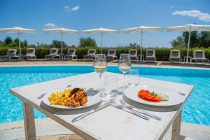 a table with food and wine glasses next to a swimming pool at Felix Hotels - Galanias Hotel & Retreat in Bari Sardo