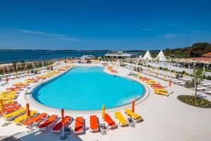 a swimming pool with chairs and umbrellas and the ocean at Arena Grand Kazela Camping Homes in Medulin