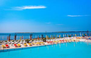 a pool with chairs and umbrellas next to a beach at Arena Grand Kazela Camping Homes in Medulin