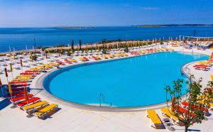 a large swimming pool with chairs and umbrellas and the ocean at Arena Grand Kazela Camping Homes in Medulin