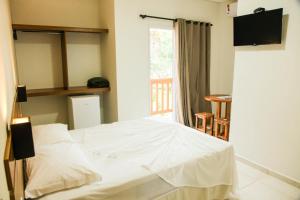 a white bed in a room with a window at Pousada Canto da Praça in Bertioga