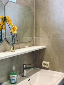 a bathroom sink with a mirror and a vase with yellow flowers at Sunlit Apartment with Garden, Next to Station, Vienna in Vösendorf