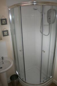 a shower with a glass door next to a sink at Castaway Cabin in St Merryn