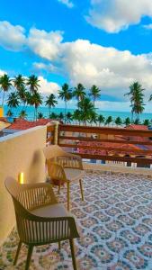 a patio with two benches and palm trees and the ocean at Japaratinga Suites in Japaratinga
