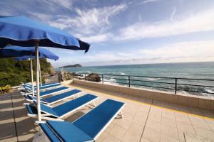 a row of lounge chairs with an umbrella and the ocean at Hotel La Scogliera in Cavi di Lavagna