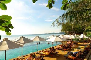 ein Strand mit Stühlen und Sonnenschirmen und Menschen im Wasser in der Unterkunft Camia Resort & Spa in Phu Quoc