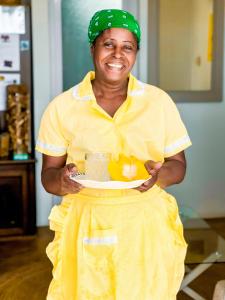 a woman in a yellow dress holding a plate of food at Lakaz Kreol 2 Soupir Tourist Residence in Port Mathurin