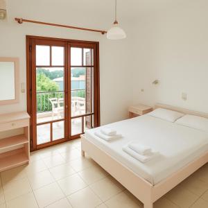 a white bedroom with a bed and a balcony at Captain Michalis Apartments - 750m from Kalamaki Beach in Galatás