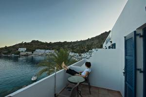 a person sitting on a balcony looking at the water at Nikolas Rooms in Loutro